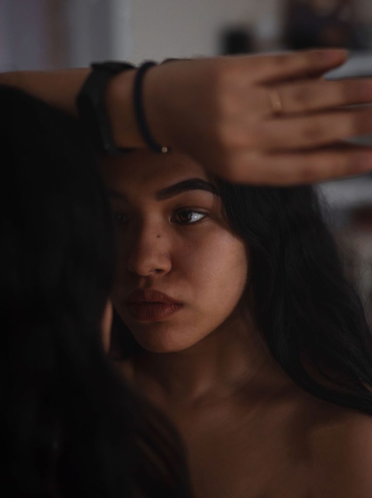 Unsmiling Latino woman looking at reflection in mirror