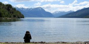 Girl sitting at the edge of a lake in Tierra del Fuego national park with mountains in the background.