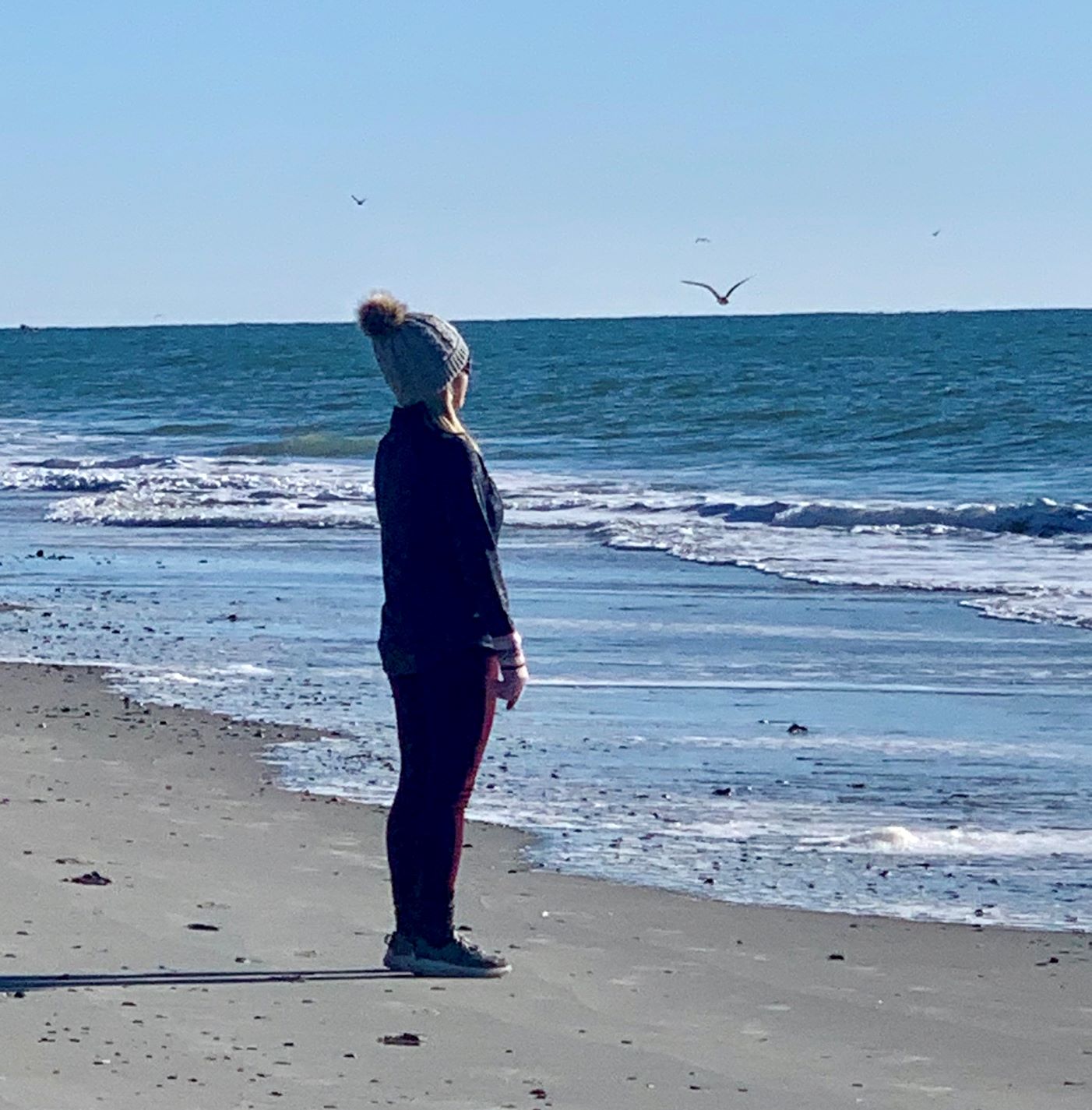 Jackie J.Reid wearing winter hat and gloves looking out at ocean